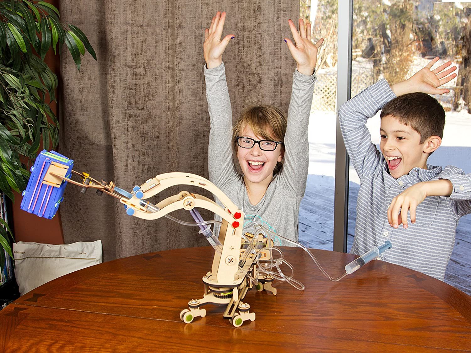 Two kids cheering as their hydraulic crane they built lifts a block